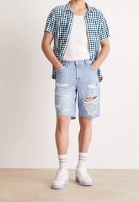 Sininen ja valkoinen ruudullinen lyhythihainen paita, valkoinen toppi, kuluneet vaaleansiniset denim-shortsit, valkoiset tennarit vaalealla pohjalla ja raidalliset sukat.