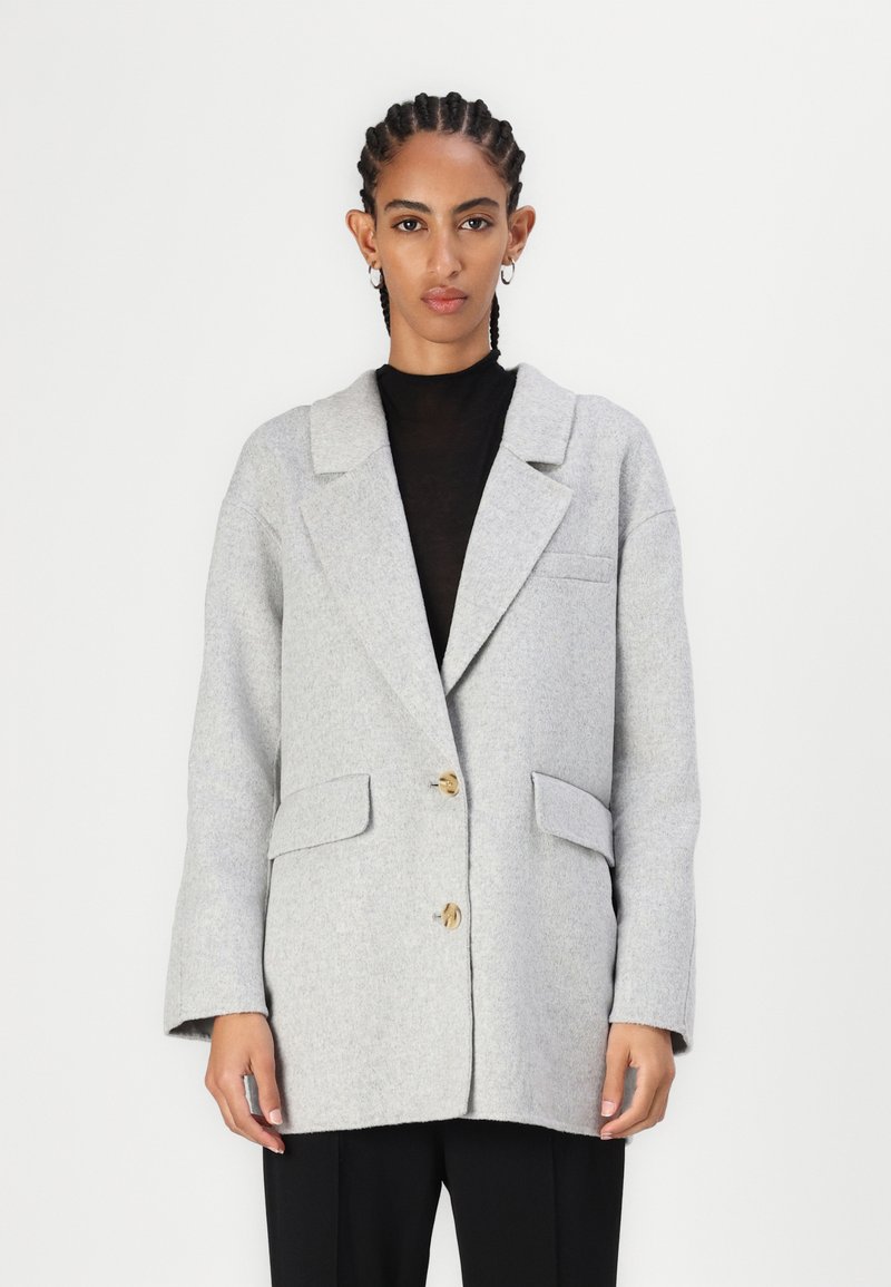Blazer de lana gris claro con cuello de muesca, dos bolsillos frontales y cierre de un solo botón. Textura suave y corte relajado.