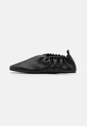 Sort blødt læder slip-on sko med elastisk ryg og spids tå, vist i sideprofil på hvid baggrund.