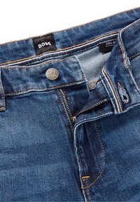 Blauwe denim jeans met een ritssluiting, metalen knoopsluiting en tan stiksels. Het "BOSS"-label is zichtbaar bij de tailleband.