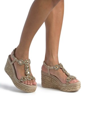 Beige wedge sandalen met een gevlochten jute zool, met een decoratieve band versierd met heldere en goudkleurige juwelen.
