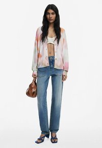 Multicolored lightweight cardigan with buttons, paired with high-waisted denim jeans, blue strappy sandals, and a brown woven handbag.