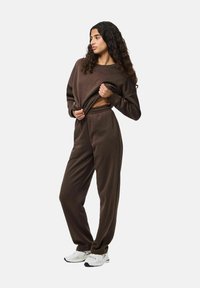 Bruine gematchte sweatshirt en broek van zacht materiaal, met een relaxte pasvorm en een elastische tailleband, gecombineerd met witte sportschoenen.