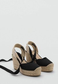 Pantofi wedge din țesătură neagră, cu un stil espadrille. Prezintă o talpă din iută împletită, spate deschis și curele din satin negru. Textură netedă cu vârfuri rotunjite.