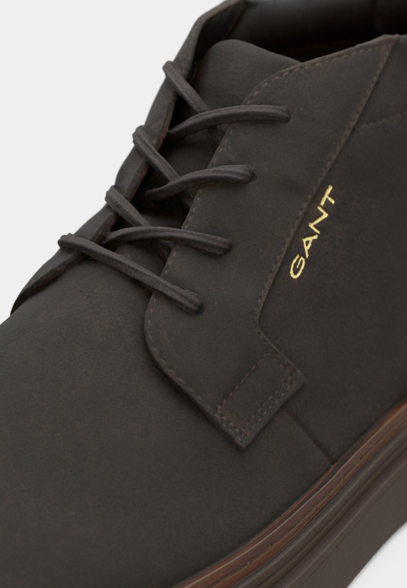 Chaussure en cuir marron à lacets avec bout rond, minimalisme de couture et logo doré en relief sur le côté. Semelle durable avec une finition texturée.