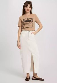 Brązowa grafika t-shirt z napisem, w połączeniu z białą spódnicą dżinsową z przodu rozciętą, noszoną z czarnymi plecionymi balerinami. Proste akcesoria w zestawie.