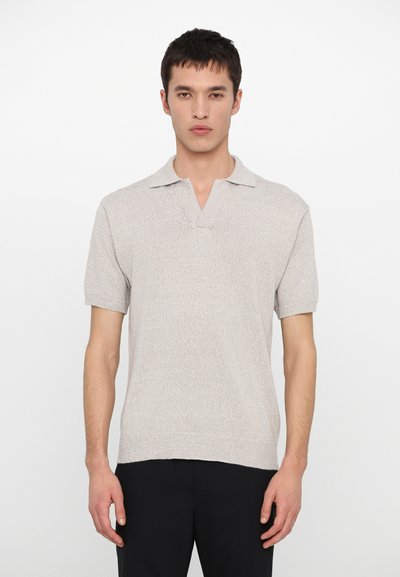 Lichtgrijze polo met korte mouwen van een gebreide textuur, voorzien van een kraag en een rechte zoom. Draagt bij zwarte broek.