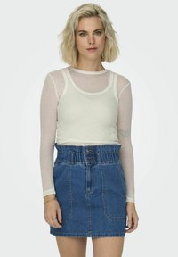 Top alb cu dungi, cu mânecă lungă, stratificat peste un maiou crem ajustat. Asortat cu o fustă din denim albastră, cu talie înaltă, elastică și cu nasturi.