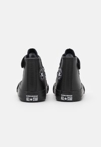 Para czarnych skórzanych trampek Converse All Star w stylu high-top widocznych z tyłu na białym tle.