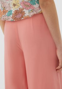 Lichtroze, wijde broek gemaakt van een gladde stof. De tailleband is ontworpen voor comfort, gecombineerd met een top met bloemenpatroon.