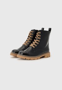 Bottines en cuir verni noir avec des lacets marron et des œillets en or. Elles disposent d'une semelle en caoutchouc avec un profil texturé pour une meilleure adhérence.