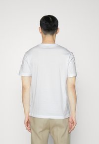 Biała bawełniana koszulka z krótkim rękawem, z okrągłym dekoltem i prostym dołem, z boczną metką na dolnej lewej stronie.