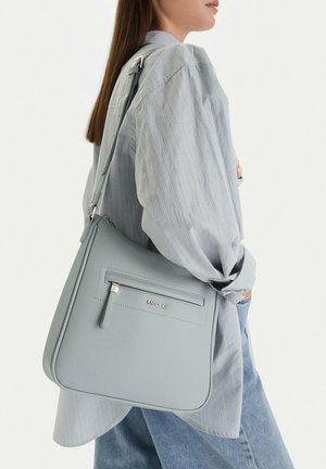 Mujer con una camisa de rayas y jeans que lleva un bolso de hombro Lasocki azul claro con un bolsillo frontal con cremallera.