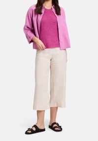 Chemise en lin rose boutonnée portée sur un débardeur en maille magenta, associée à un pantalon large crème et des sandales noires à enfiler avec des garnitures décoratives.