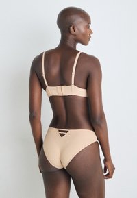 Beige bra and panty set, featuring adjustable straps, hook closure, and a cut-out detail on the panty. Smooth texture and seamless design.
