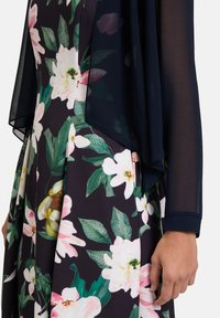 Blumenkleid mit einem dunklen marineblauen, transparenten Überzug. Es hat große rosa Blüten und grüne Blätter, mit glatter Textur und sanftem Drapierungsdesign.