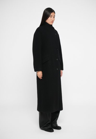 Melnas vilnas mētelis ar augstu apkakli, pogu aizdari un divām priekšējām kabatām. Mētelim ir teksturēta apdare un gara, brīva silueta.