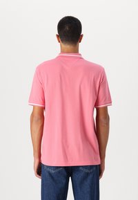 Rosa piké-skjorte med krage, hvit trim på ermene, laget av myk stoff. Vist fra baksiden, kombinert med mørkeblå jeans.