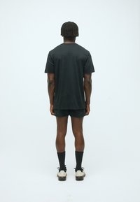 Chemise noire à manches courtes avec une coupe décontractée, dotée d'un ourlet arrondi et de petits détails de design au dos, associée à un short sombre et des chaussettes noires.