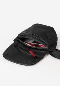 Schwarze Lederhandtasche mit Klappverschluss, ausgestattet mit einem roten Akzent-Reißverschluss und einem Innenmuster im Gitterdesign. Enthält zwei Druckknöpfe und einen Schulterriemen.