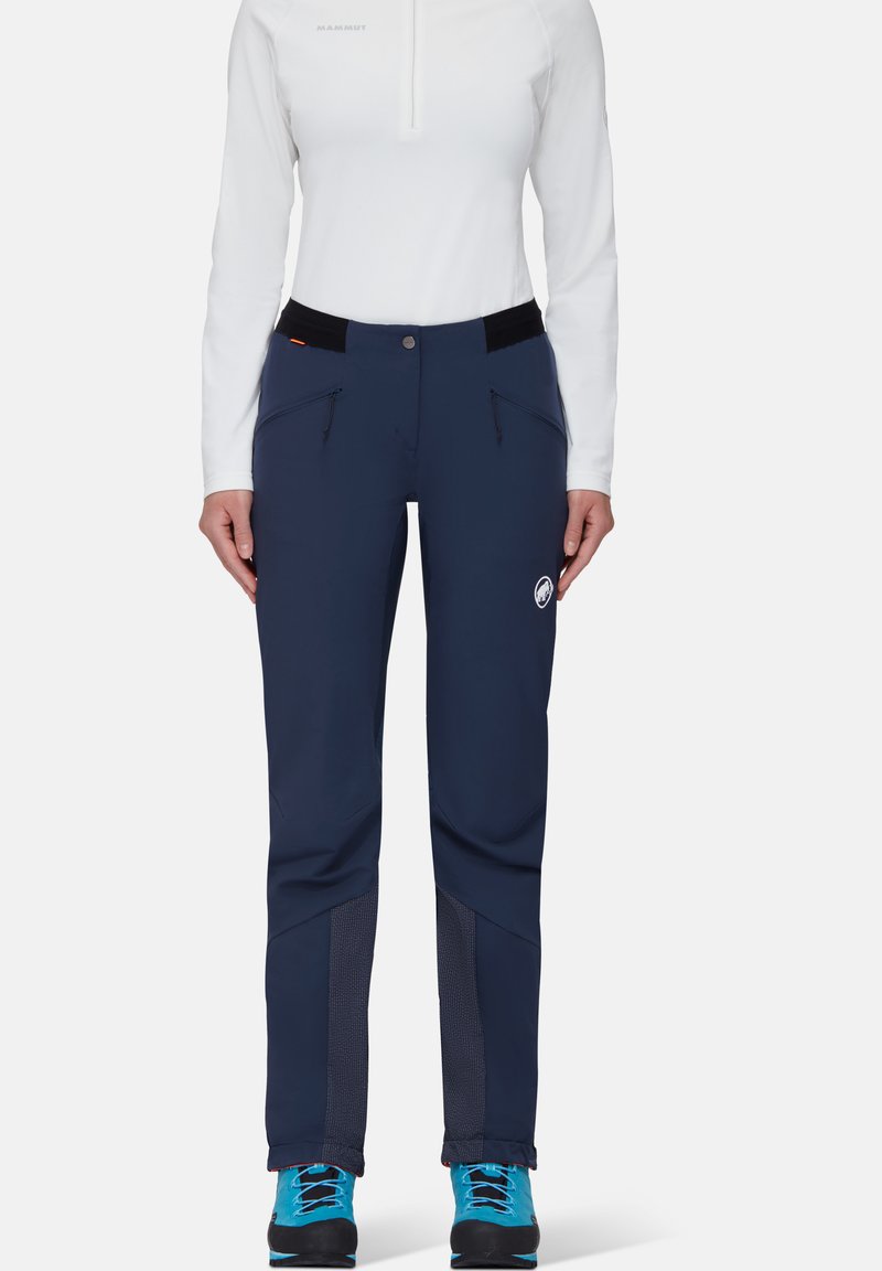 Marineblauwe broek met een aangesloten ontwerp, gemaakt van rekbaar materiaal. Beschikt over twee ritszakken, contrasterende gaaspanelen bij de enkels en een logo.