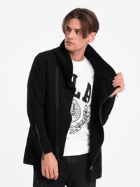 Sort zip-jakke med høj krave, der har sideskaber og en glat tekstur. Båret over en hvid grafisk T-shirt og sorte jeans.