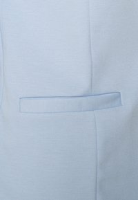 Light blue fabric with a textured surface, featuring a concealed pocket and clean lines, creating a streamlined appearance.