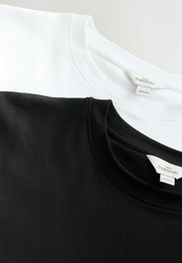 Zwei Schwangerschafts-T-Shirts: eines weiß und eines schwarz, Baumwollstoff, Rundhalsausschnitt, sichtbare Etiketten mit Marken- und Pflegeinformationen.