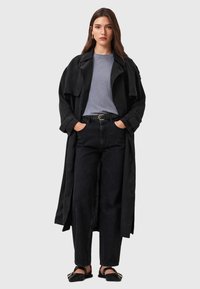 Abrigo negro sobre una camiseta gris, combinado con pantalones vaqueros negros de cintura alta. Completado con sandalias planas negras con un acento dorado.