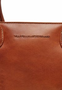 Borsa a tote in pelle marrone con logo del marchio impresso, texture liscia e cuciture rinforzate lungo i bordi.