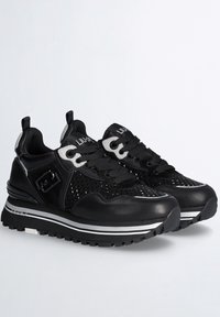 Zapatillas negras y grises con cordones, con costados perforados, suelas gruesas y estampadas, y detalles de marca en la lengüeta y el talón.