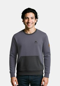 Grauer Sweatshirt mit einer dunkler grauen Tasche, gerippten Bündchen und Rundhalsausschnitt. Verfügt über ein Logo auf der Brust und ein Patch am Ärmel.