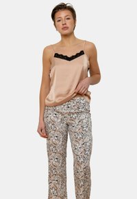 Camisole en satin rose clair avec des finitions en dentelle noire, assortie à un pantalon à motifs floraux dans des teintes blanches, noires et roses.