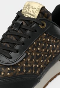 Μαύρο αθλητικό παπούτσι με χρυσές λεπτομέρειες, διαθέτει δερμάτινο επάνω μέρος, πλευρές με σχέδια και τρουκς. Κλείνει με κορδόνια και έχει μεταλλική γλώσσα με λογότυπο.