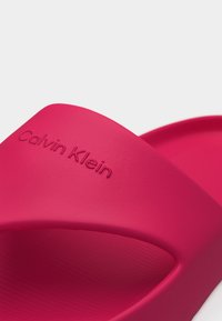 Φωτεινό ροζ σανδάλι slide Calvin Klein με ανάγλυφο όνομα επωνυμίας στο φαρδύ λουράκι και υφή στην επένδυση ποδιού.