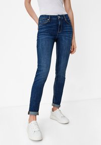 Tmavě modré džíny skinny se středním pasem, obsahující přední kapsy, poutka na pásek a ohrnuté manžety. Nosené s bílými teniskami.