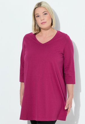 Magenta Tunika mit V-Ausschnitt und dreiviertel Ärmeln, aus weichem Stoff gefertigt. Die Länge reicht bis zur Mitte des Oberschenkels und hat einen lässigen Schnitt.