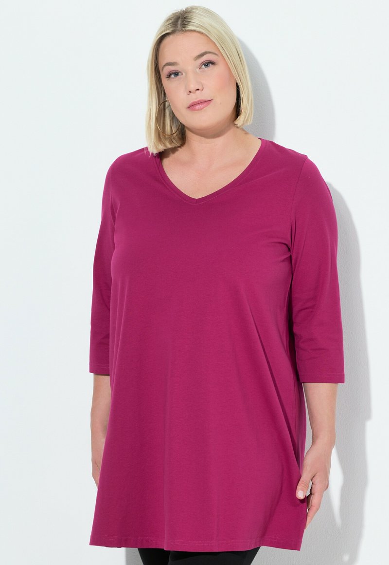 Magenta Tunika mit V-Ausschnitt und dreiviertel Ärmeln, aus weichem Stoff gefertigt. Die Länge reicht bis zur Mitte des Oberschenkels und hat einen lässigen Schnitt.