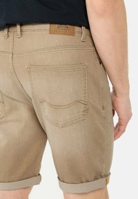 Shorts kaki avec ourlets retournés, fabriqués en denim. Dotés de deux poches arrière et d'un patch en cuir portant l'étiquette "tissu actif".