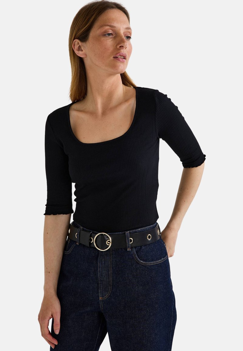Haut noir à fines côtes avec un décolleté carré et des manches trois-quarts. Associé à un jean en denim noir taille haute et une ceinture noire avec une boucle circulaire en or.