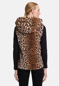 Kamizelka w cętki z kapturem, wykonana z miękkiego materiału; pod nią znajduje się czarna bluzka z długim rękawem oraz dopasowane czarne spodnie.