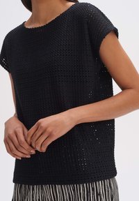 Top nero lavorato a maglia con una vestibilità ampia, caratterizzato da un motivo testurizzato e maniche corte, abbinato a un indumento inferiore a righe.