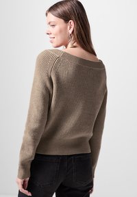 Maglione khaki a coste con scollo ampio, tessuto testurizzato e orlo aderente. Abbinato a jeans scuri, presenta una silhouette rilassata.