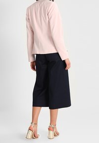 Světle růžový přiléhavý blazer, navy široké kalhoty a metalické sandály na vysokém podpatku. Blazer má hladkou texturu s minimem švů.