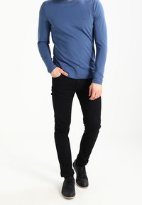 Modrá košile s dlouhým rukávem a decentním logem, spárovaná s černými slim-fit kalhotami a černými botami. Hladký materiál a přiléhavý střih.