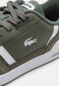 Žalios odinės sportbačiai su baltais akcentais ir perforuotu dizainu. Yra pilkos raišteliai ir baltas krokodilo logotipas šone.