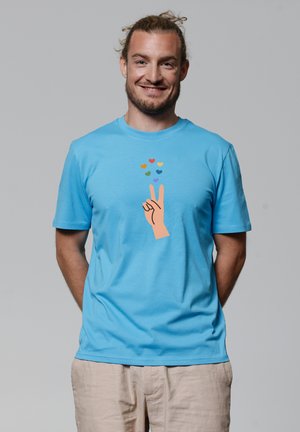 Lichtblauw katoenen T-shirt met een grafisch ontwerp van een hand die een vredesteken maakt, omringd door kleine kleurrijke harticonen.