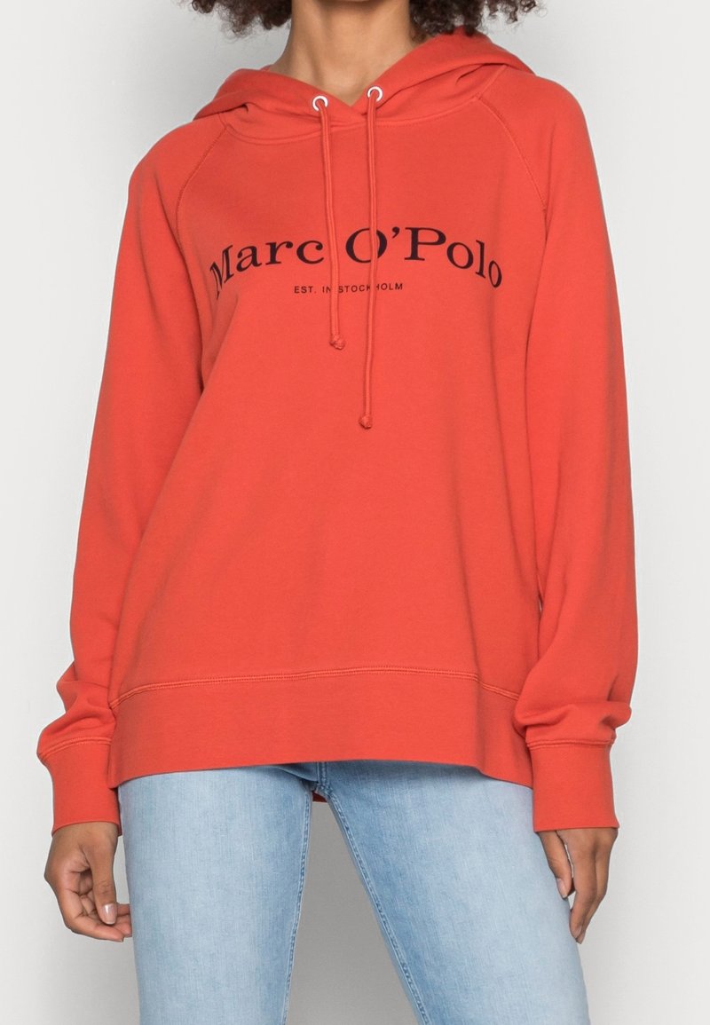 Felpa rossa con cappuccio e logo frontale, con coulisse e polsini a costine. Tessuto morbido e vestibilità comoda. Abbinata a jeans azzurri chiari.