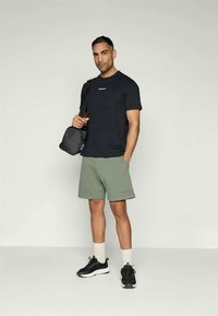 Tmavomodré tričko, zelené šortky, čierne tenisky, sivá taška. Krátke rukávy, voľný strih, minimálne logo na tričku a šortkách.