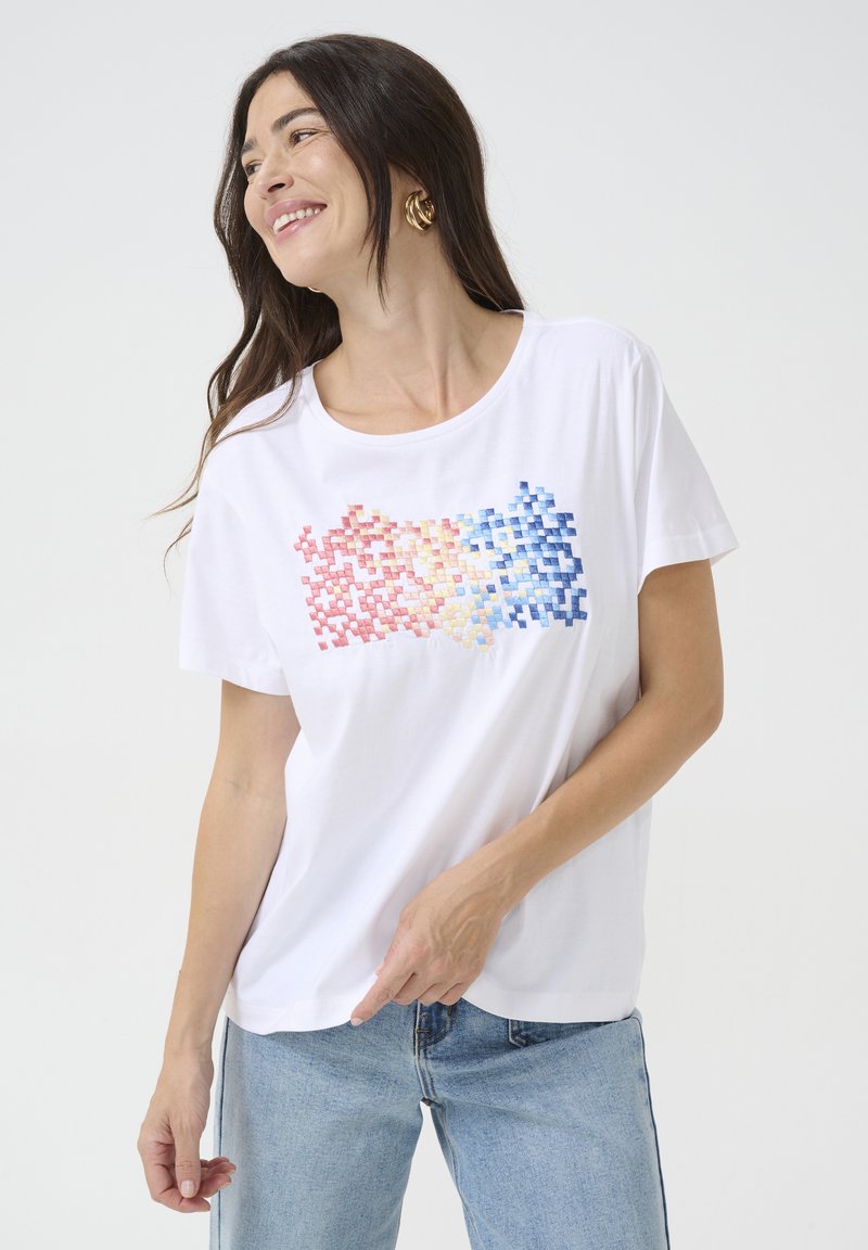 T-shirt en coton blanc arborant un design de dégradé pixelisé en rouge, rose, jaune et bleu. Manches courtes et encolure ronde.